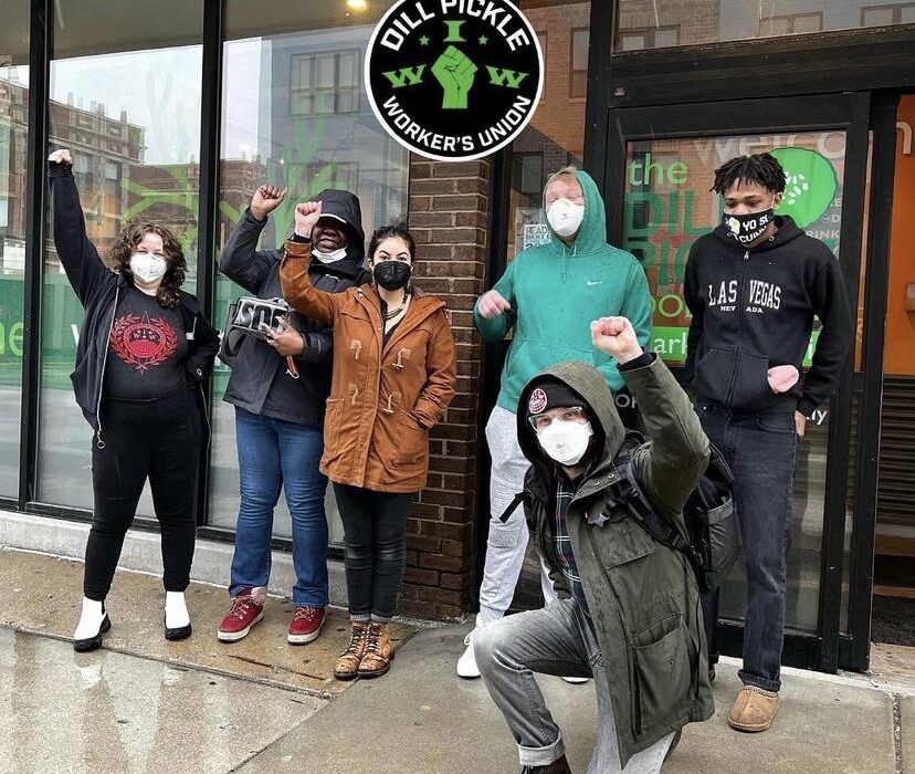 Group photo Dill Pickle Worker's Union members standing in front of the shop with their fists raised