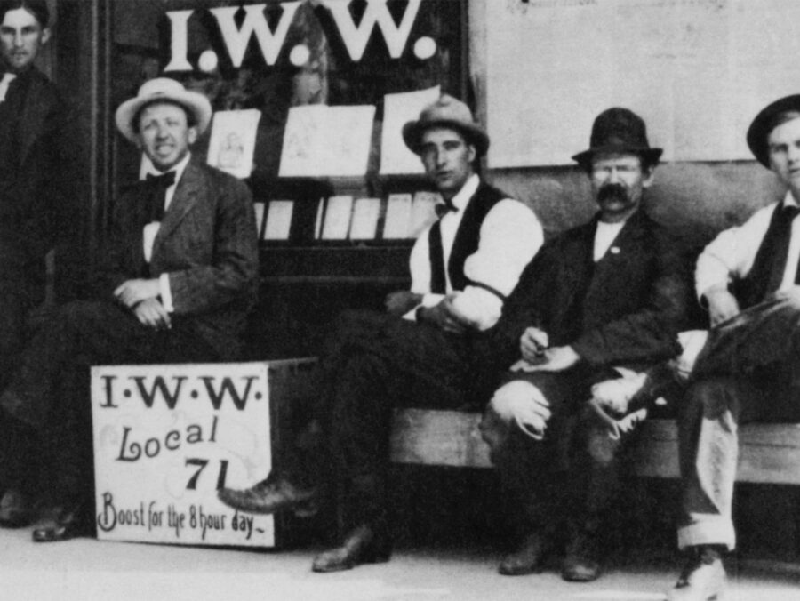 Photo of IWW Local 71, featuring union members sitting on a bench in front of a union hall