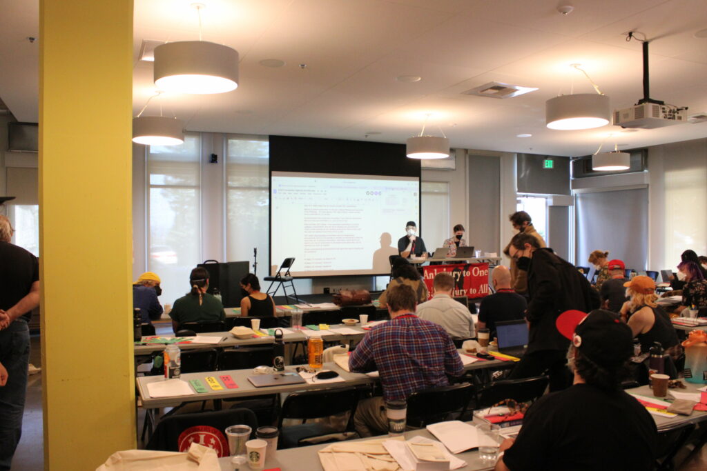 Convention in session in Seattle. Several people wearing masks in a conference room. Porco Rossellini 2023.