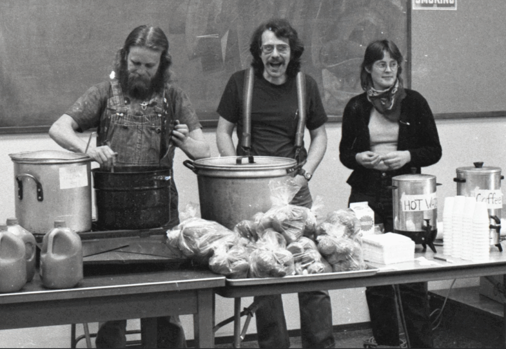 Fellow Workers David Helm, Scott Slaba, and Mary Thurtle serve food from a table. Food for People Soup Kitchen, Bellingham IWW. From the IWW Materials Preservation Project.