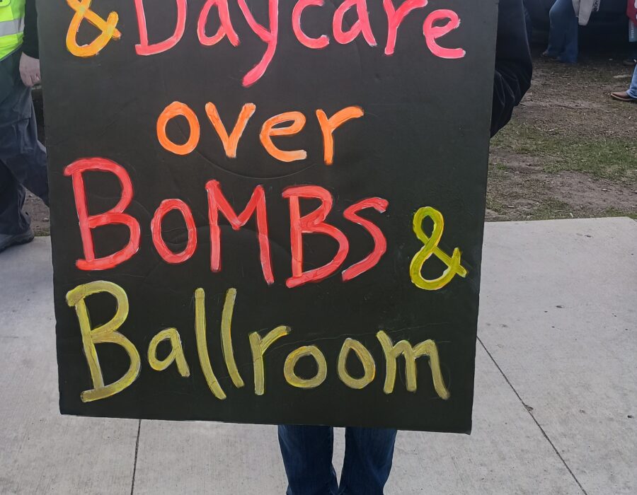 Photo of a person holding a sign that says "Healthcare and Daycare over Bombs and Ballroom."